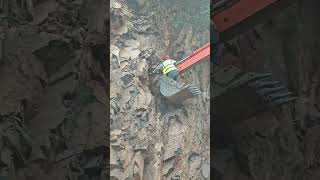 A worker on the bucket of a crawler excavator pulls something out of a rock with the bucket [upl. by Tirreg]